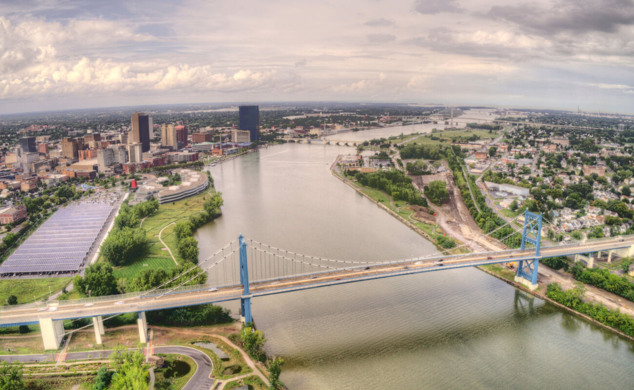 aerial view of downtown Toledo Ohio and neighboring areas in the distance, while the river and a suspension bridge are in the foreground